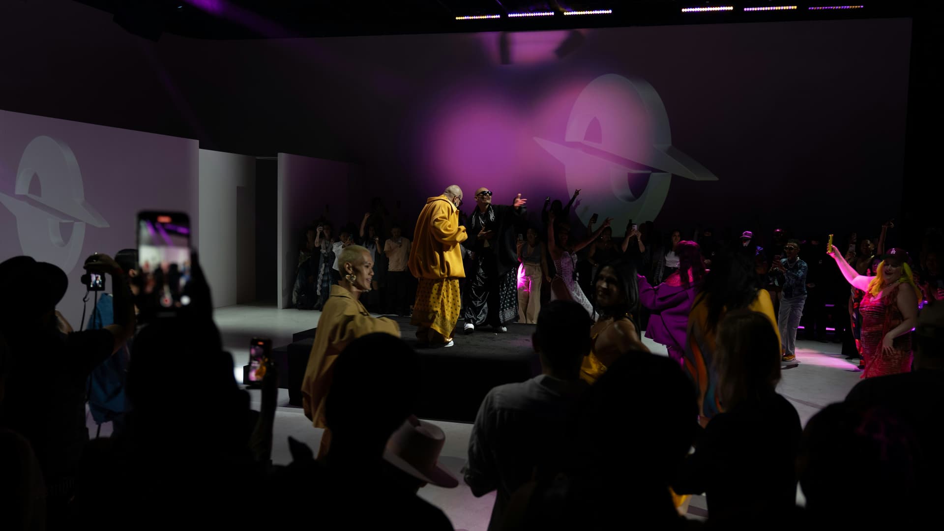 A performer in patterned couture on a dimly lit runway
