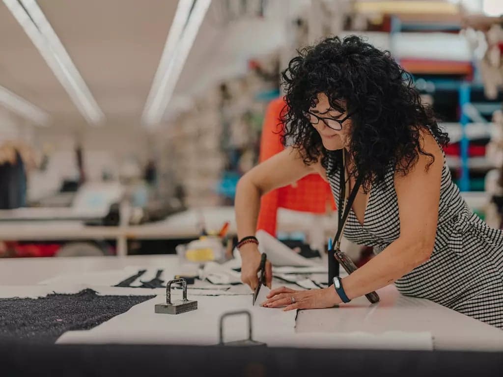 A designer cutting patterned fabric with tailor’s shears on a studio table