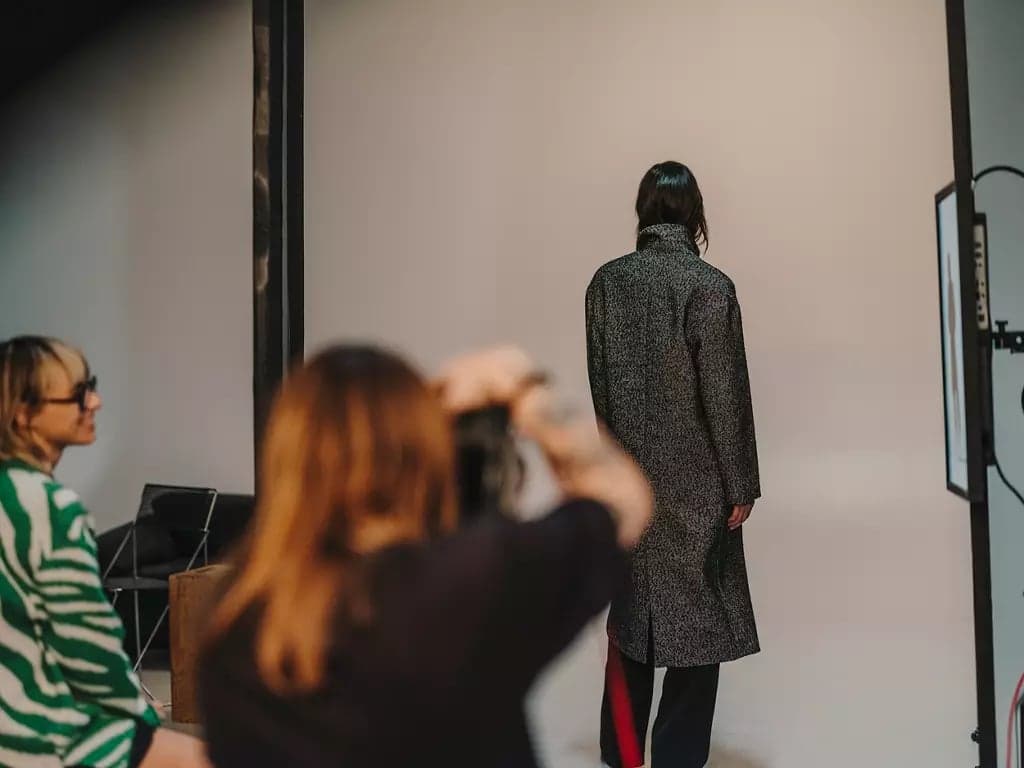 A photographer shooting a model in a textured overcoat against a studio backdrop