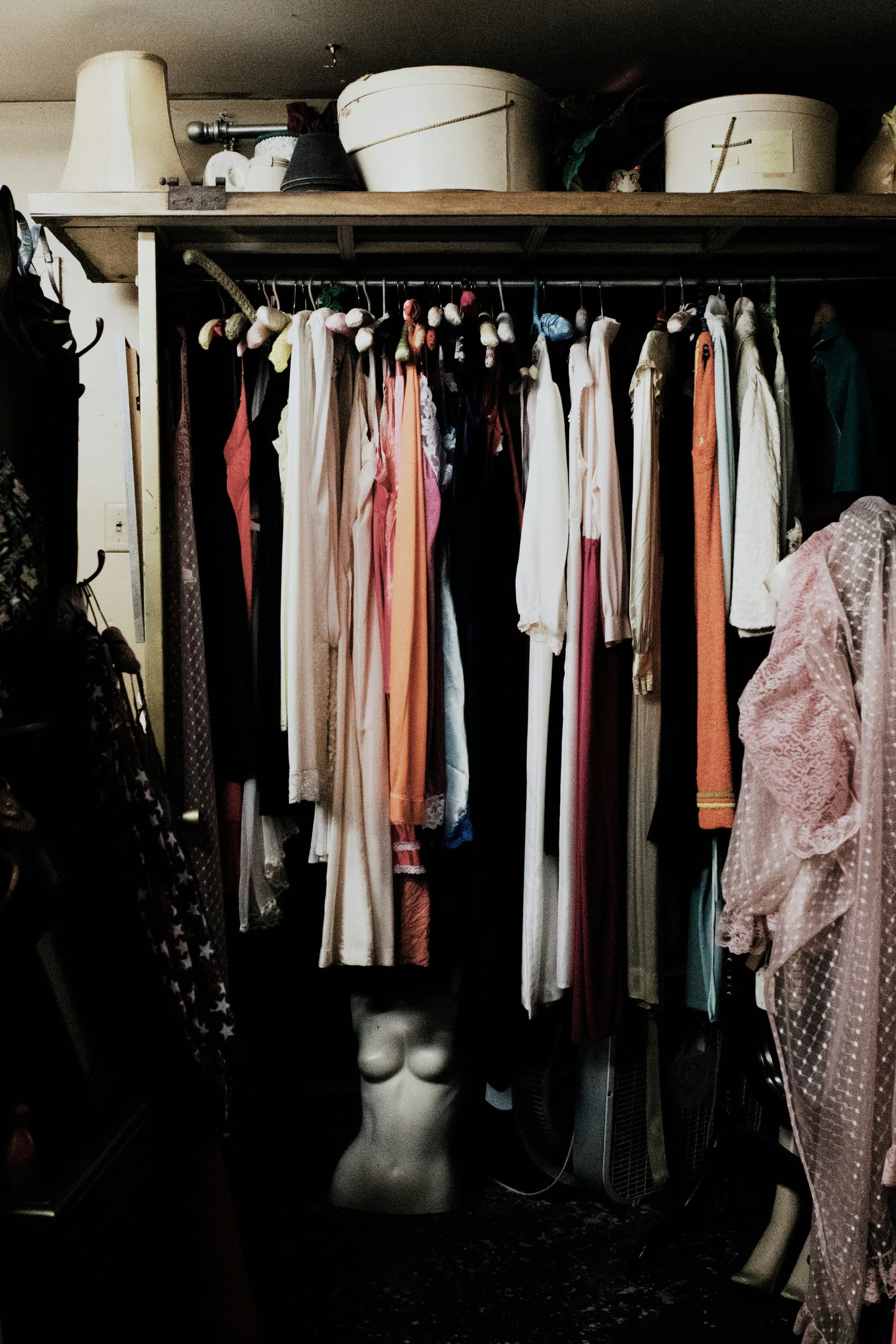An open closet packed with hanging clothes, boxes, and a mannequin torso